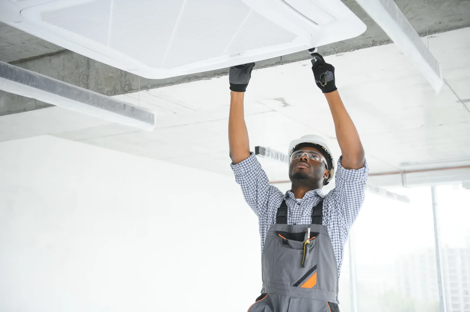 African technician installing a smoke detector on a ceiling